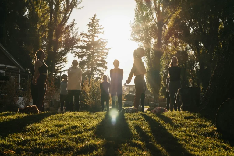 Groupe debout dans l'herbe à contre-jour pour une séance de yoga en plein air