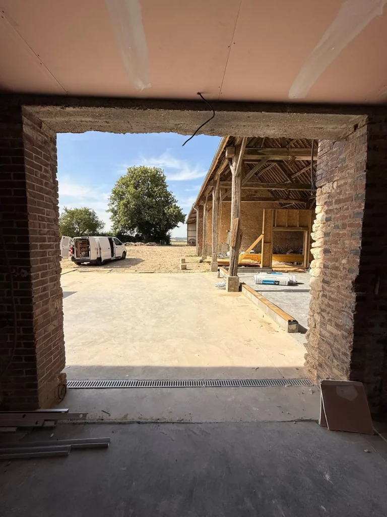 Vue sur la charpente ancienne et la campagne du Perche depuis l'intérieur de la grange