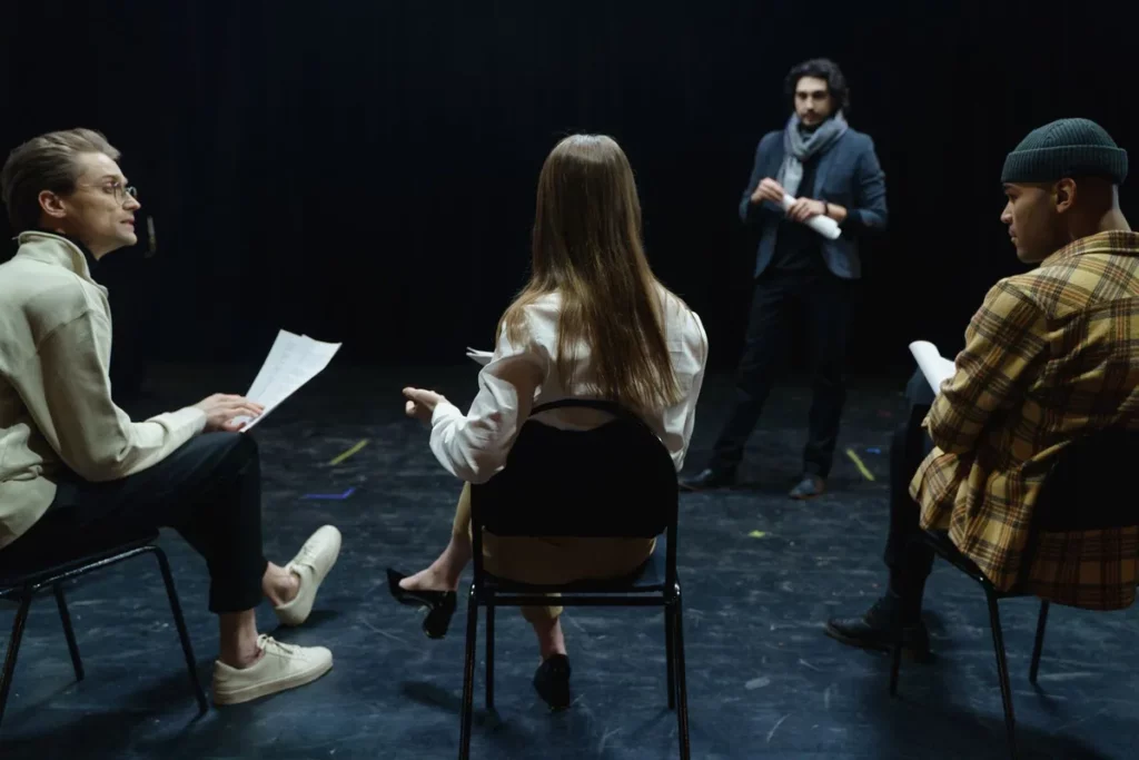 Compagnie de théâtre en répétition avec sa metteuse en scène, texte en main
