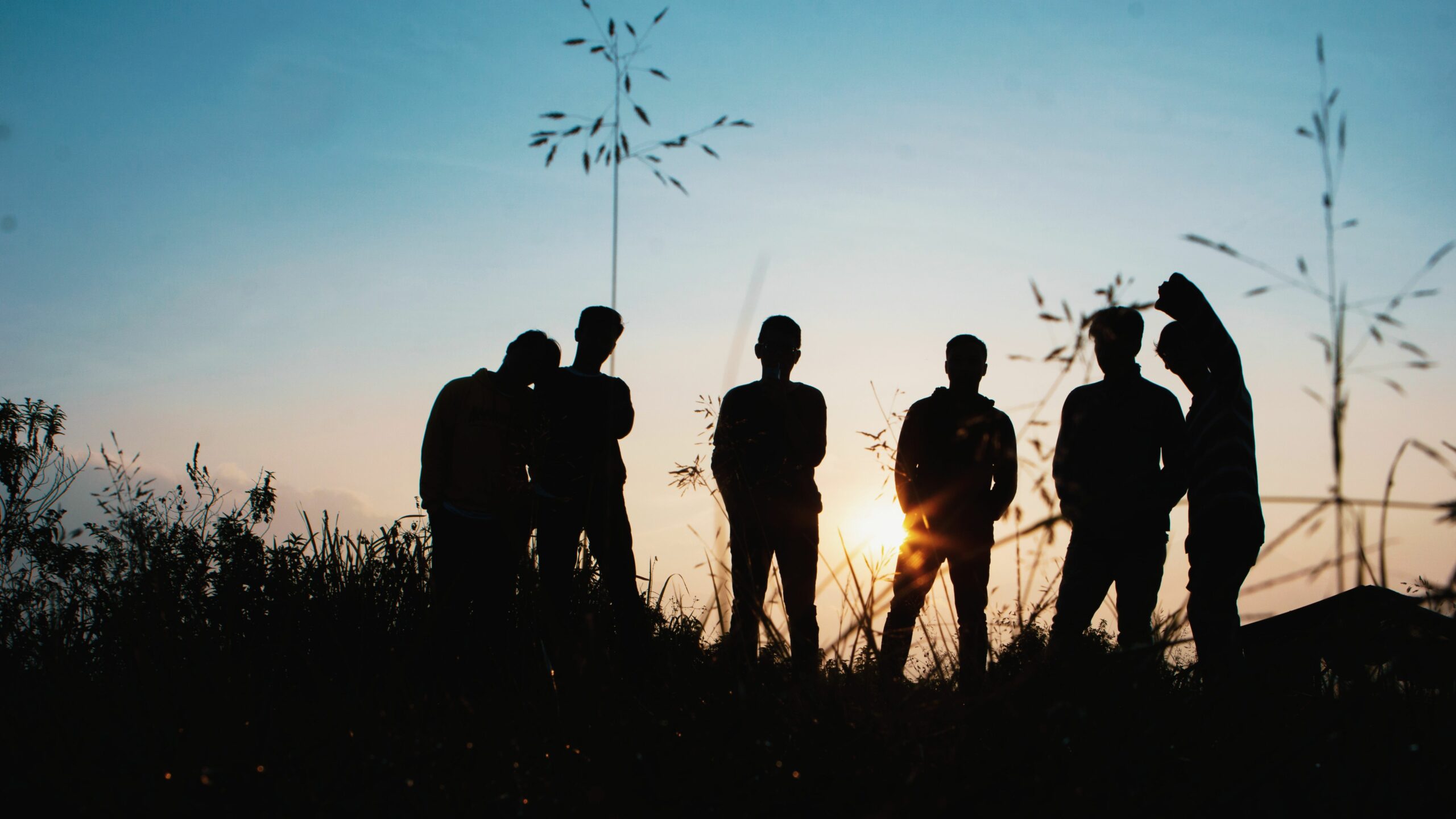 Groupe de personnes en silhouette debout sur un terrain en herbe au coucher du soleil
