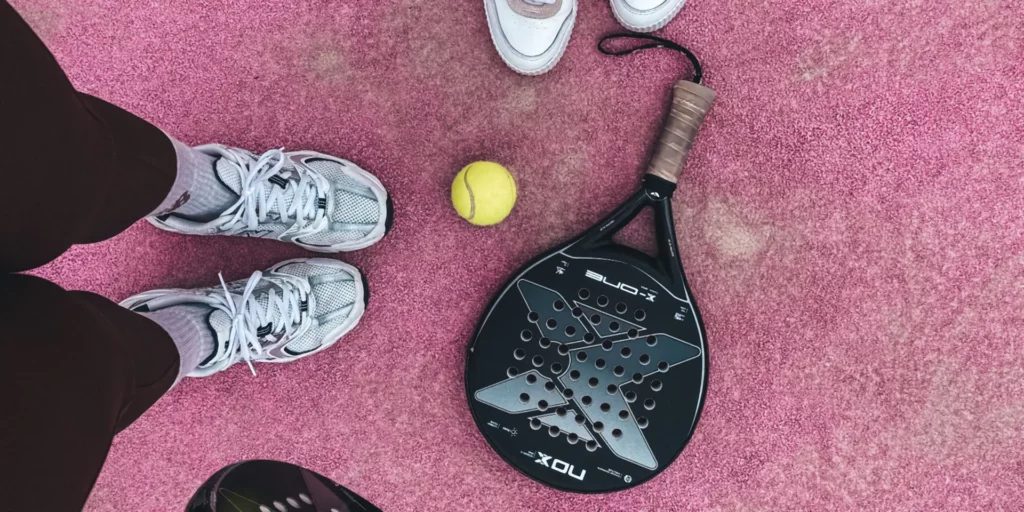 Raquettes de padel et balle posées sur un court de padel rose
