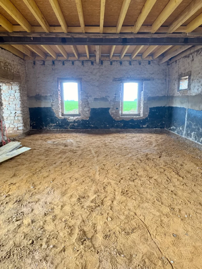 Espace de réception de la Villa Perchée en travaux : sol en terre battue, solives neuves et 2 fenêtres sur les champs
