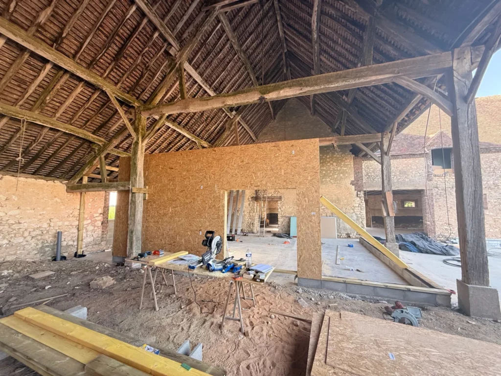Salle festive en chantier sous la charpente ancienne de la grange, cloisons en bois en cours de pose