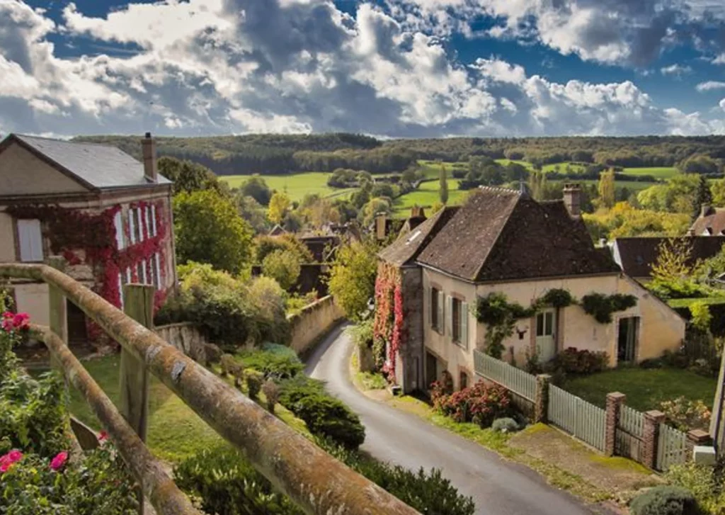 Village du Perche : maisons en pierre couvertes de vigne vierge, ruelle en pente et vue sur le bocage et les forêts
